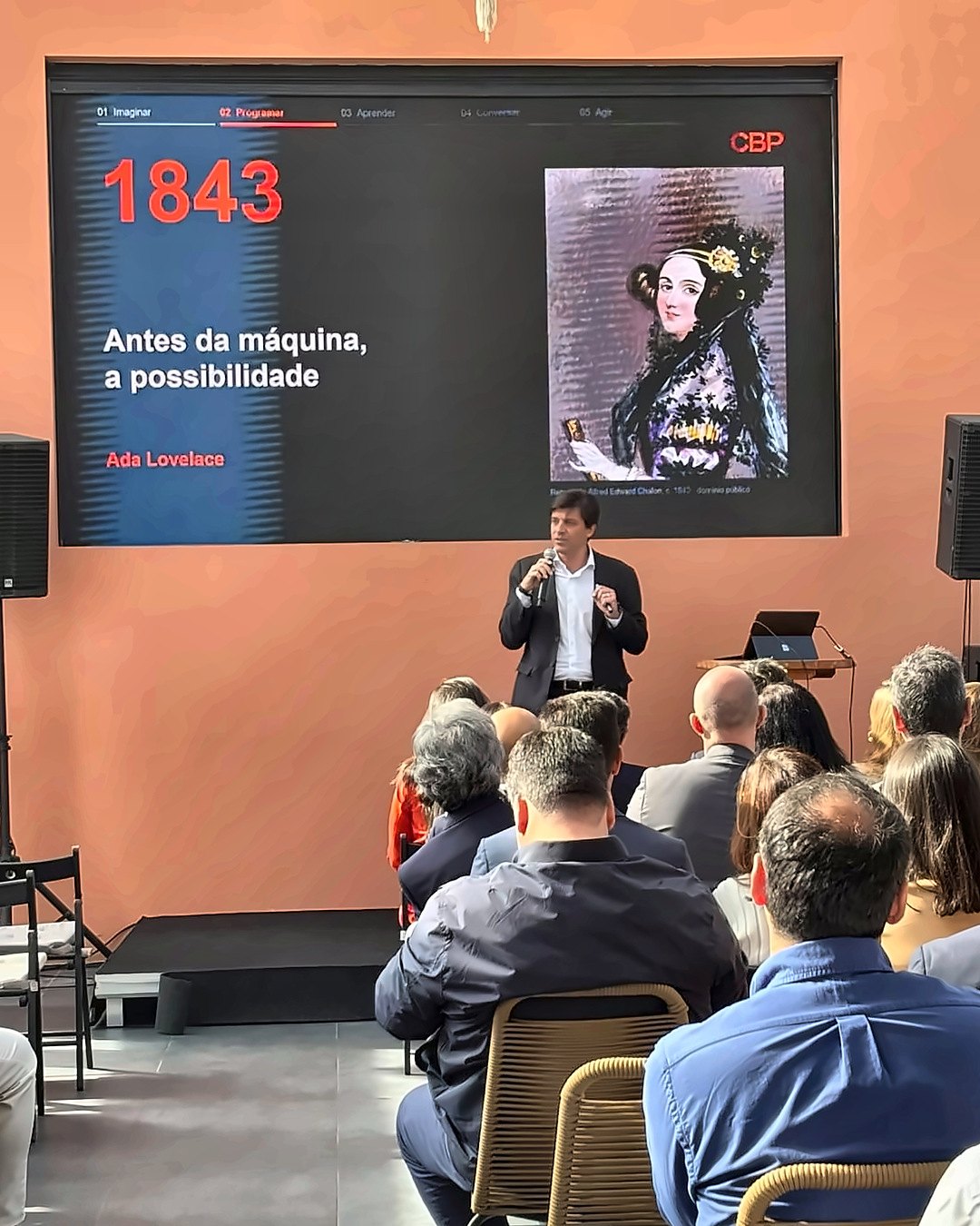 Miguel Sousa Soares em palco, diante do ecrã sobre Ada Lovelace, 1843